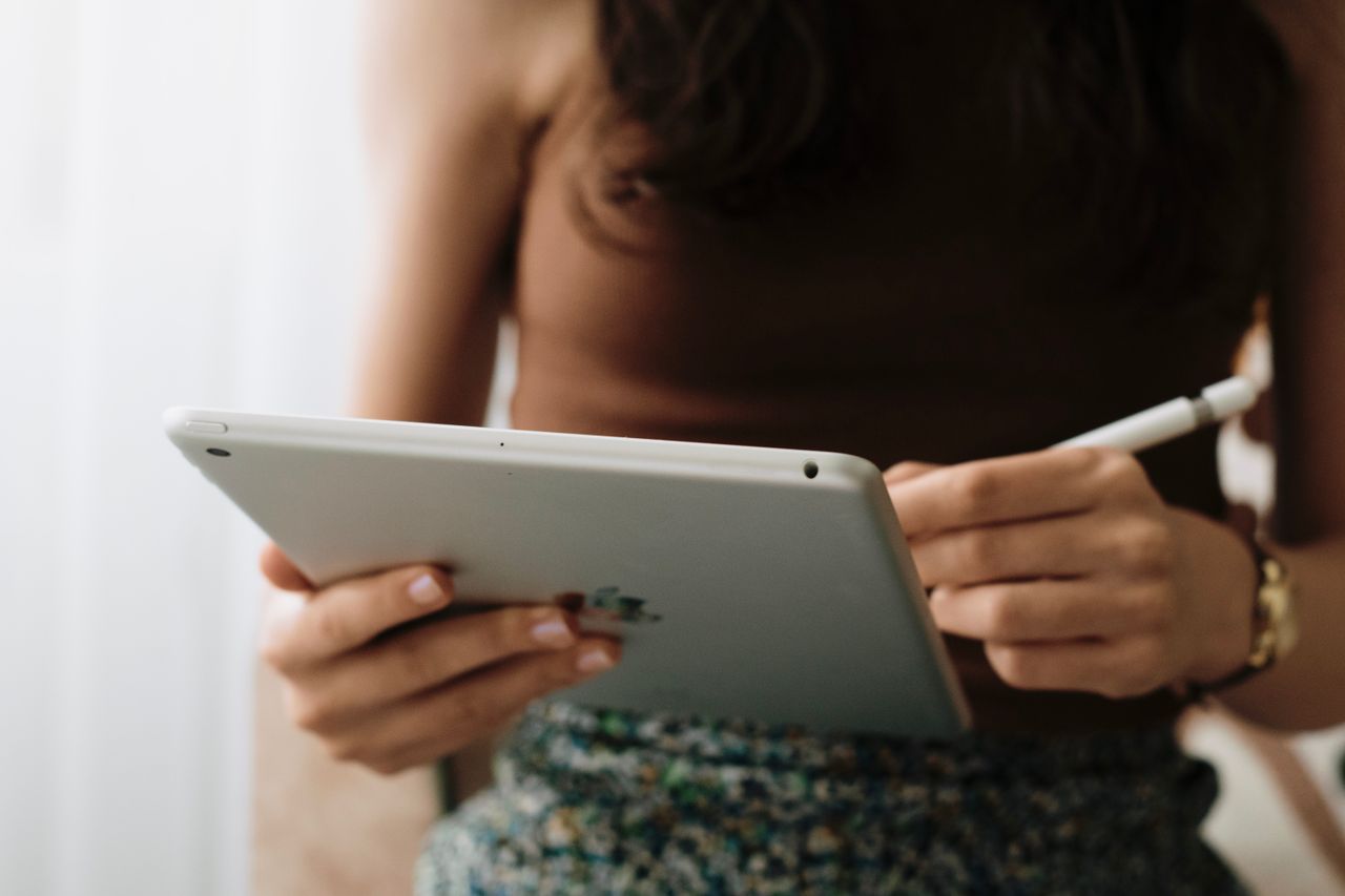 A woman using a tablet with a stylus indoors, symbolizing relaxation and modern technology.